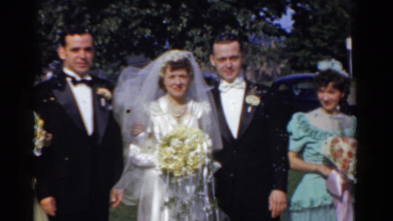 Wedding party posing outdoors with bride, groom, tuxedoed attendant, and bridesmaid holding flowers.