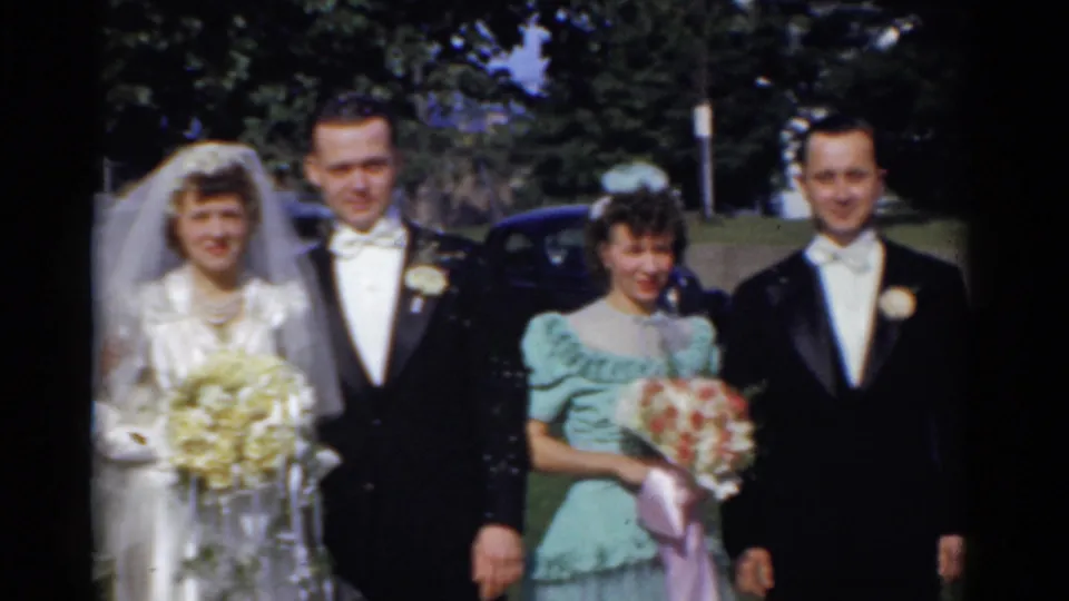 1975 Bridgeport wedding group with bride and groom centered, bridesmaid holding flowers, and a tuxedoed man at the edge of the frame.