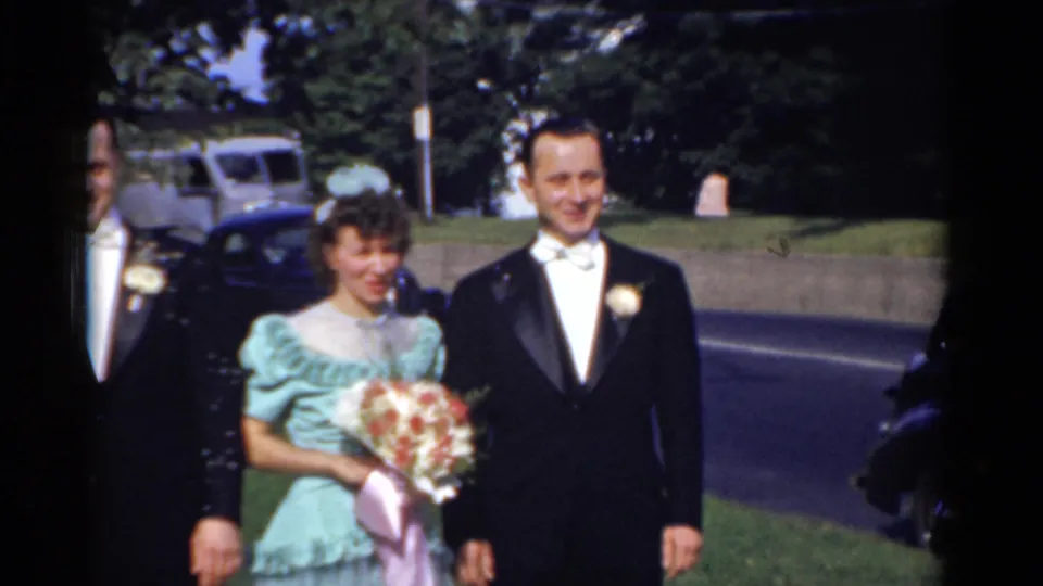 1975 Bridgeport wedding footage showing a bridesmaid with bouquet and a groom in tuxedo posing near the street.