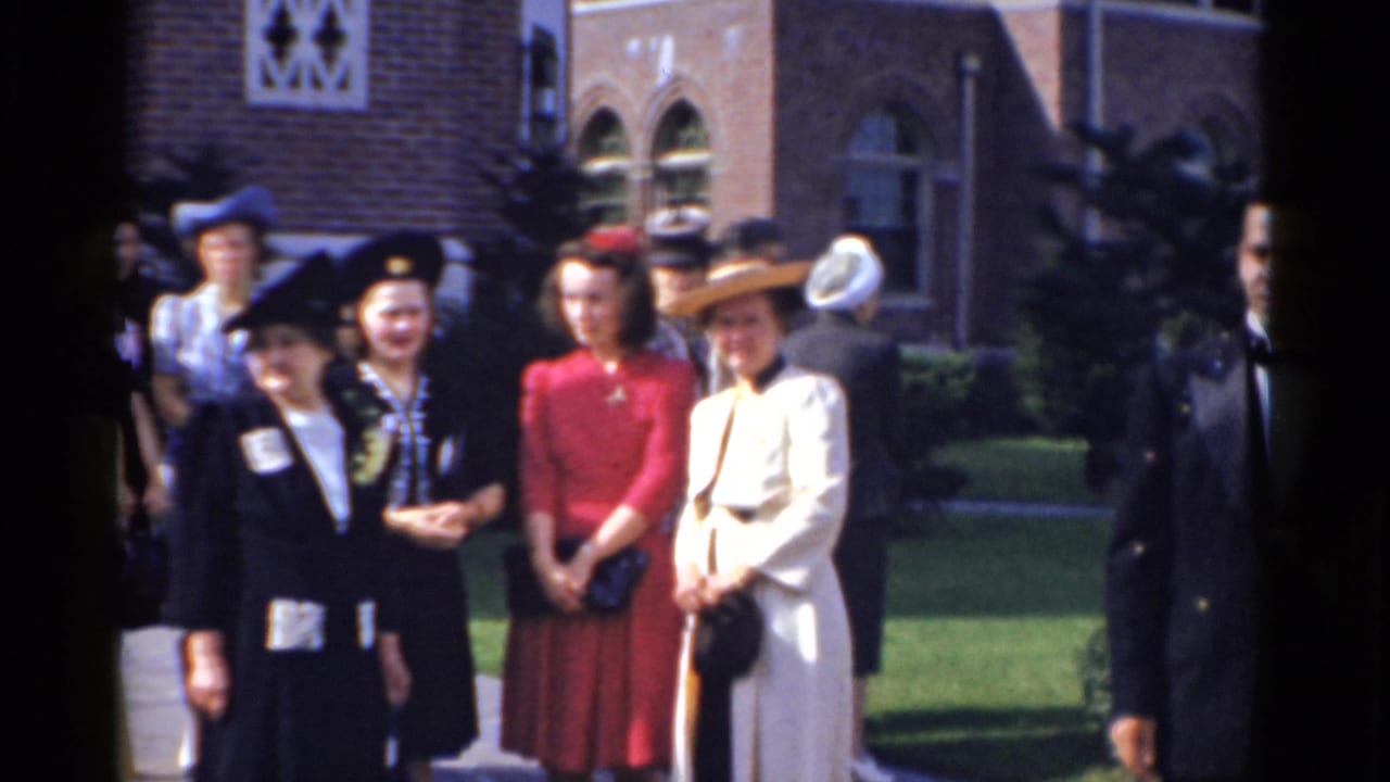Wedding guests in formal clothing stand outside a brick church.