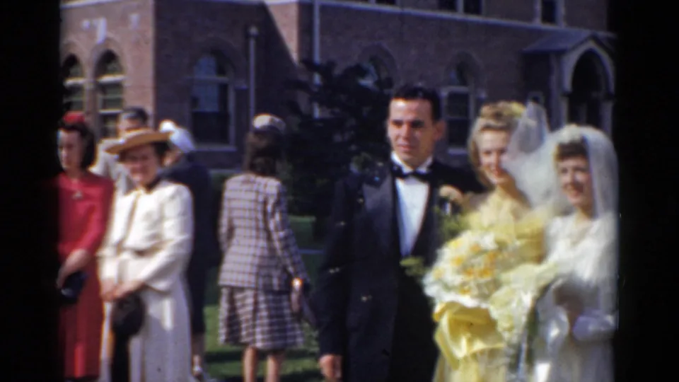 The bride in a veil appears beside the groom and attendants outside the brick church during the Bridgeport wedding scene.