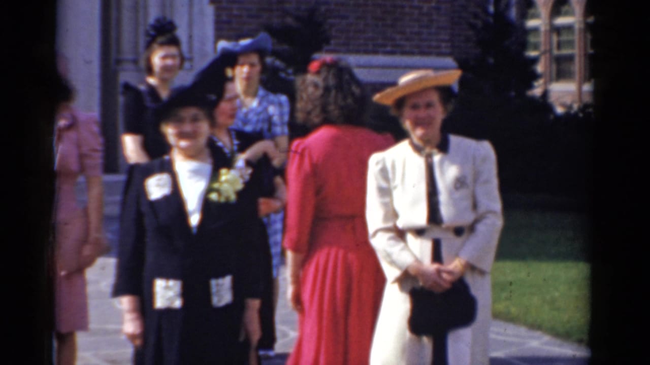 1975 Bridgeport home-movie frame of women in dresses and hats posing outside a brick building.