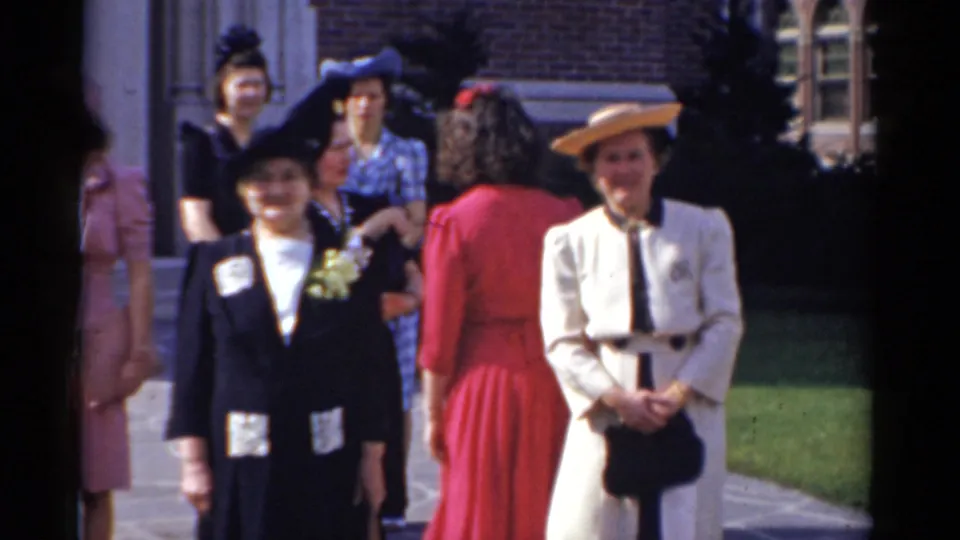1975 Bridgeport home-movie frame of women in dresses and hats posing outside a brick building.