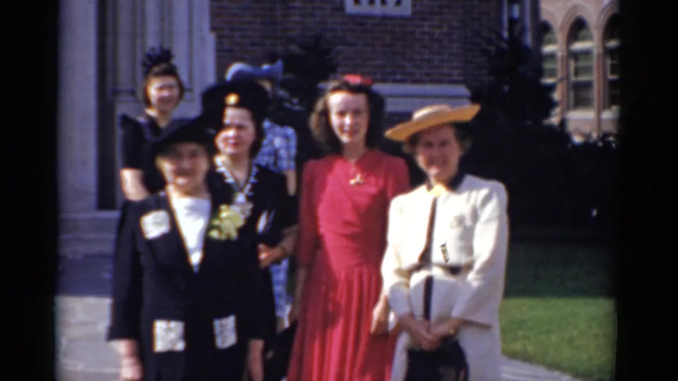 1975 Bridgeport frame of women smiling and posing together outside a brick building on 8mm film.