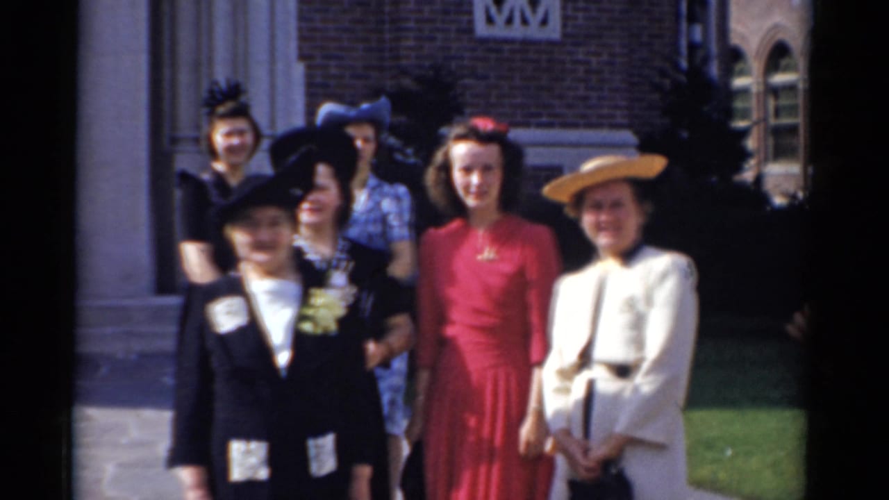 In Bridgeport, Connecticut in 1975, women in formal hats and dresses stand near a brick building while posing for a home-movie camera.