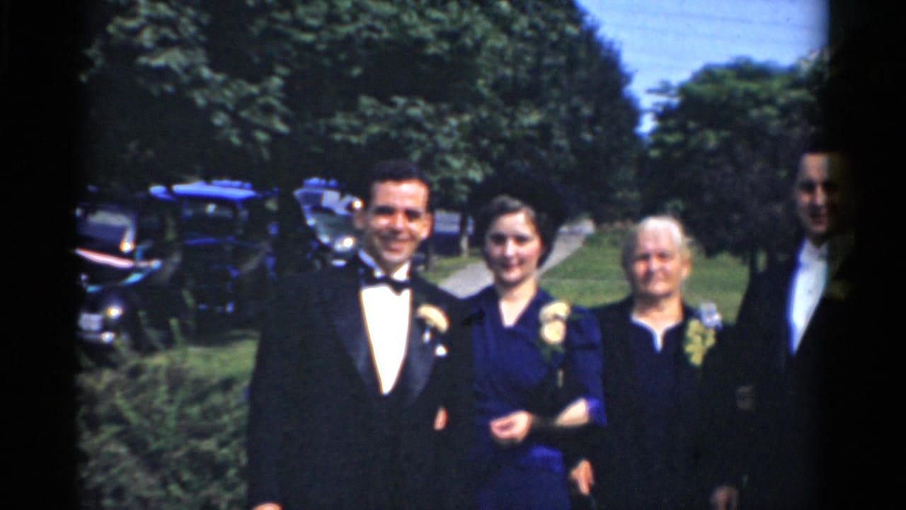 Four formally dressed adults pose outdoors on a lawn near trees and parked cars.