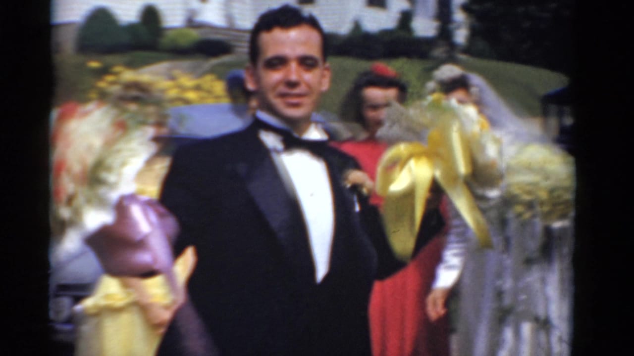 Groom faces the camera between bouquet holders outdoors.