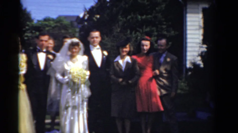 The wedding party stands in a loose outdoor lineup with the bride and groom near the center and attendants on both sides.