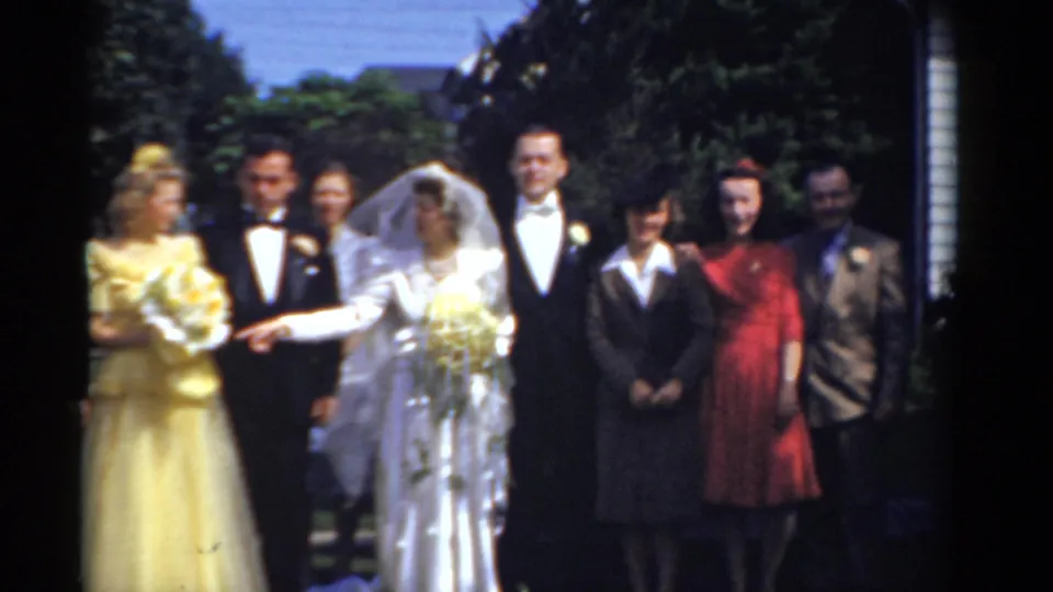 1975 Bridgeport wedding party poses outdoors, with a bride in a white gown and veil beside a groom in a tuxedo and guests in colorful formalwear.