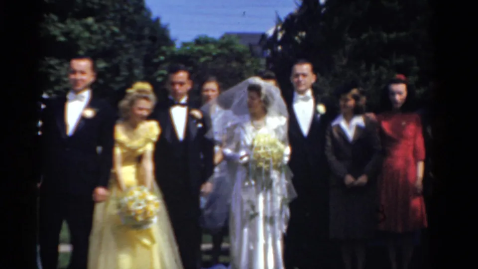 The bride in a white veil stands near the groom and formal wedding guests during an outdoor Bridgeport, Connecticut home-movie scene from 1975.