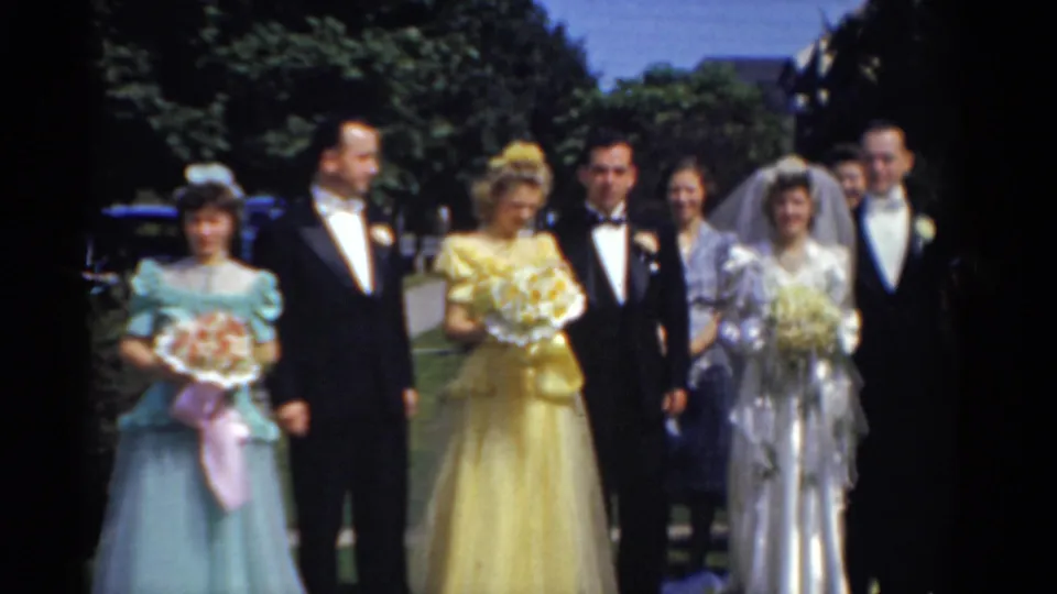 1975 Bridgeport bridal party outdoors, with the bride and groom near bridesmaids in blue and yellow gowns and men in black tuxedos.