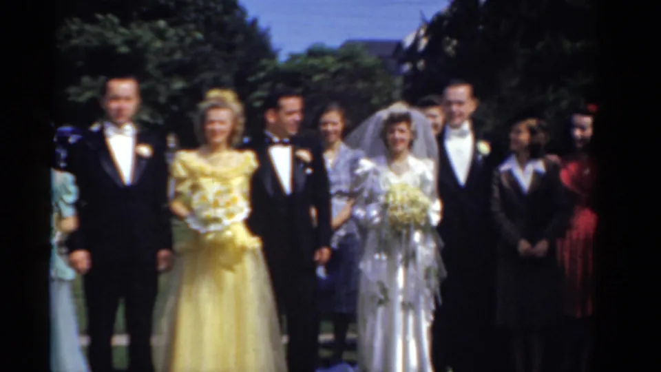 Bridgeport 1975 wedding party gathered outdoors, with the bride, groom, attendants in pastel dresses, tuxedoed men, and guests nearby.