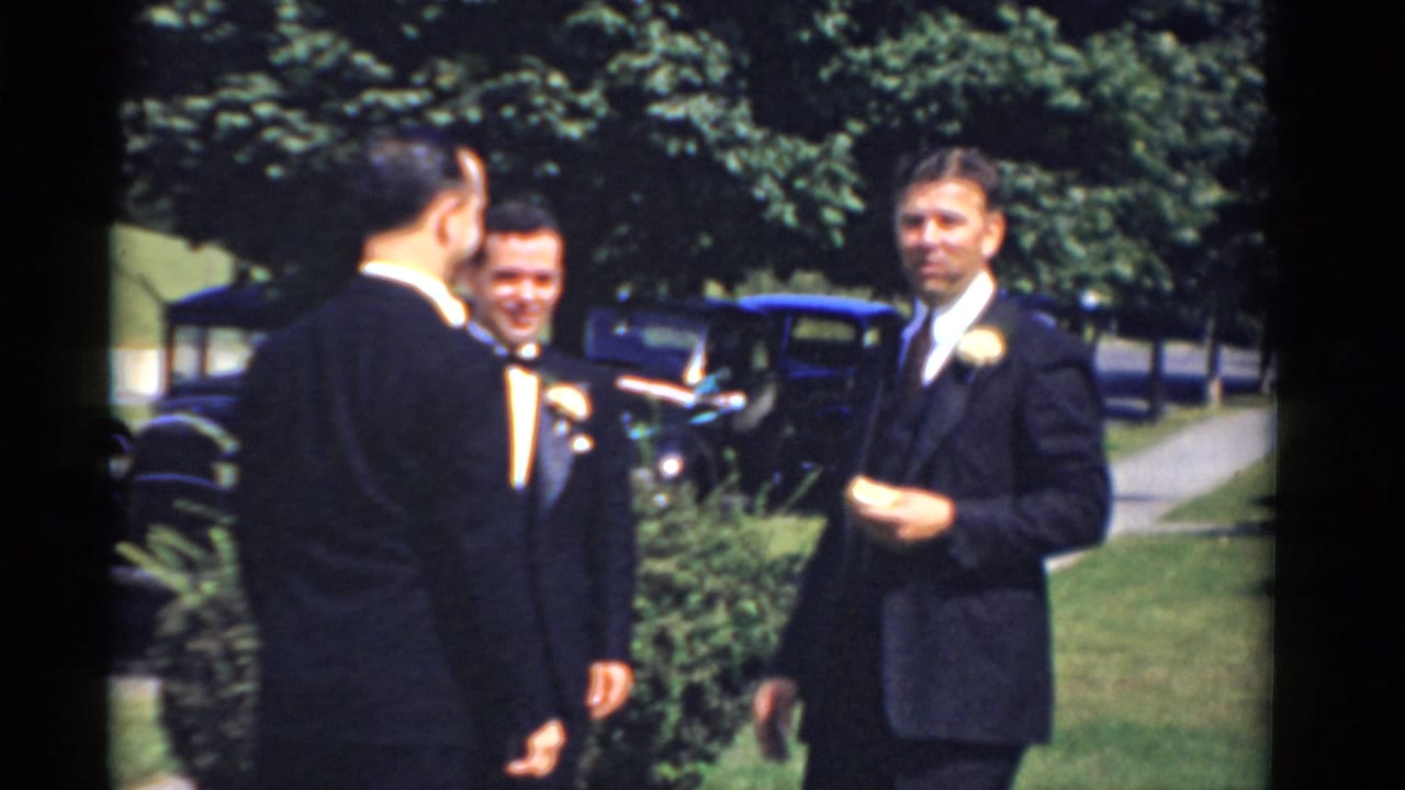 In Bridgeport, Connecticut 1975 home-movie footage, three formally dressed men gather outdoors near a lawn, trees, and vintage cars.