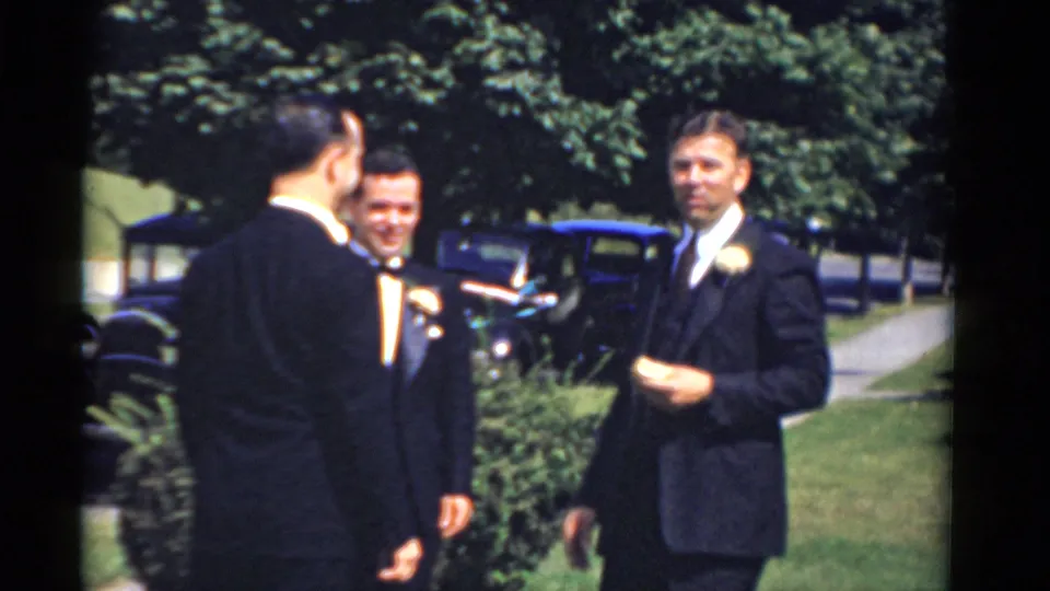In Bridgeport, Connecticut 1975 home-movie footage, three formally dressed men gather outdoors near a lawn, trees, and vintage cars.