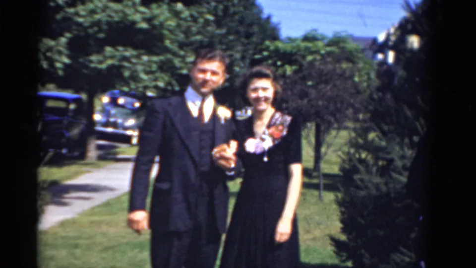 In the final 1975 Bridgeport frame, a formally dressed man and woman smile toward the camera with trees, sidewalk, and vintage cars behind them.