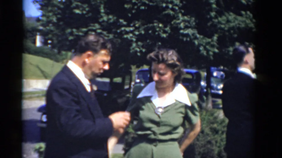 A suited man with a boutonniere stands beside a woman in a green dress with a white collar during the outdoor Bridgeport event.