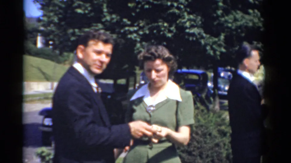In this supported 1975 Bridgeport frame, a suited man faces the camera while the woman beside him looks down during a quiet outdoor moment.