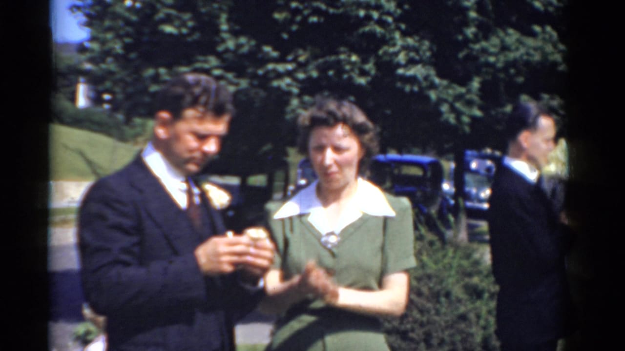 1975 Bridgeport 8mm wedding frame showing a groom beside a woman in a green dress, with parked cars and trees behind them.