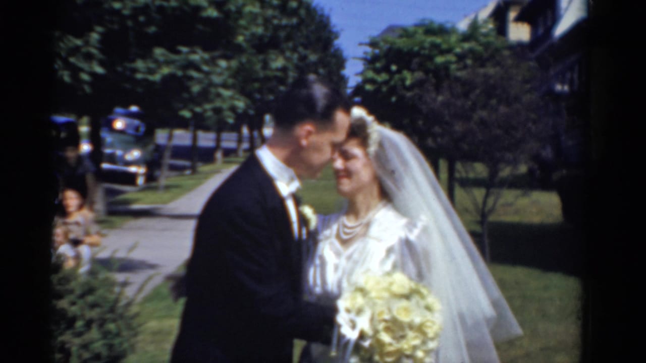Bride and groom pose closely outdoors beside a sidewalk and trees.