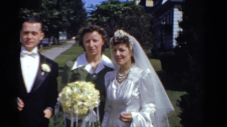The groom, bride, and a female guest pose together outdoors in 1975 Bridgeport, with trees and houses behind them.