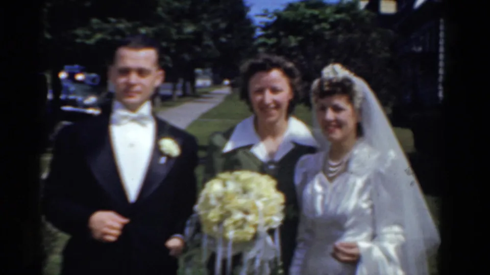The bride, groom, and female guest stand shoulder to shoulder in a sunny 1975 Bridgeport wedding home movie frame.