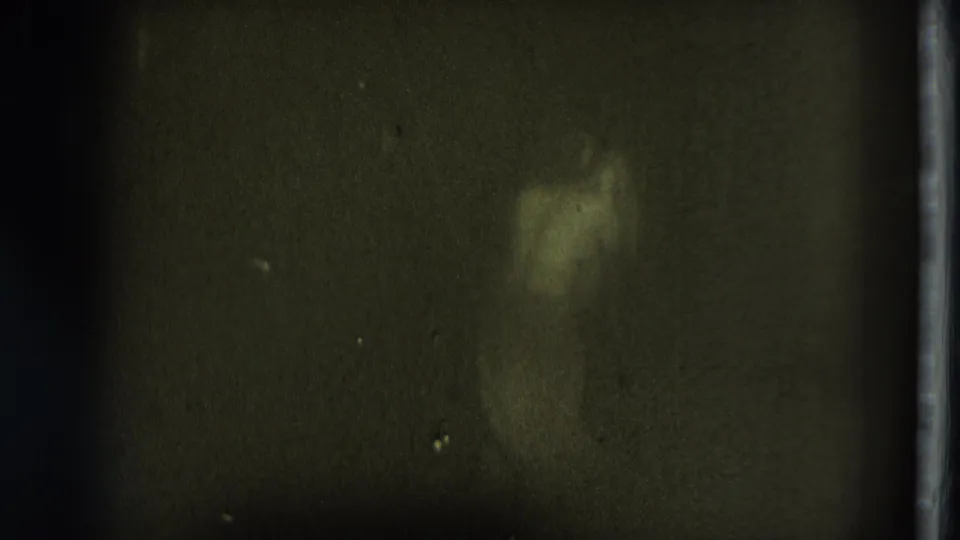 A blurred pale figure or shoulder appears near the upper right in the dim 8mm home-movie frame, with grain and frame-edge markings.