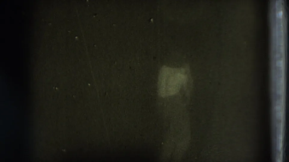 A small pale portion of the moving figure remains visible in a dark 1975 8mm frame with low exposure and pronounced grain.