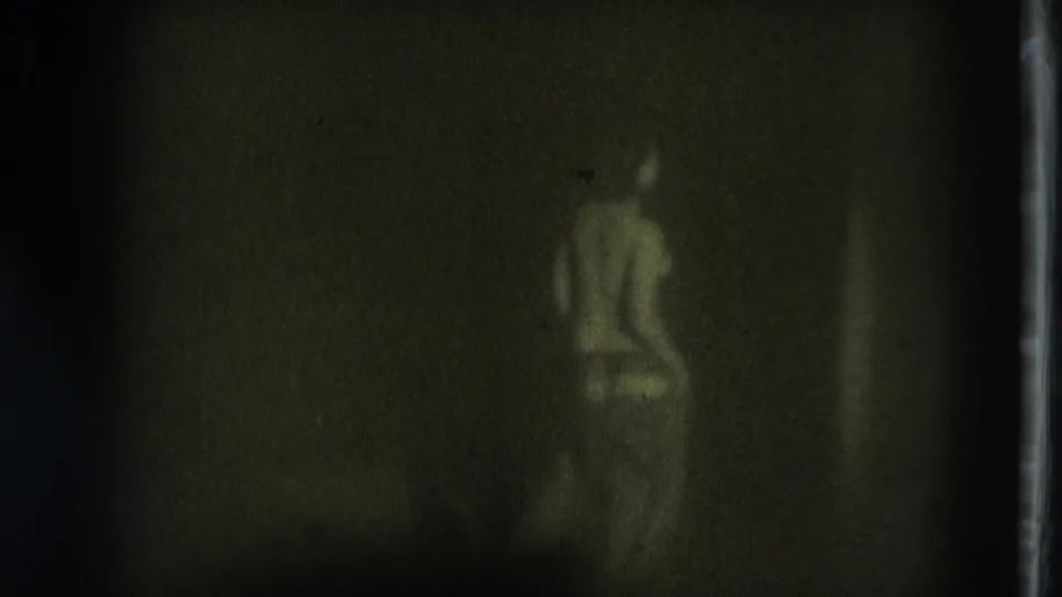 A light-clothed person stands at the right side of a dim 1975 San Francisco 8mm frame, with another faint vertical shape nearby.