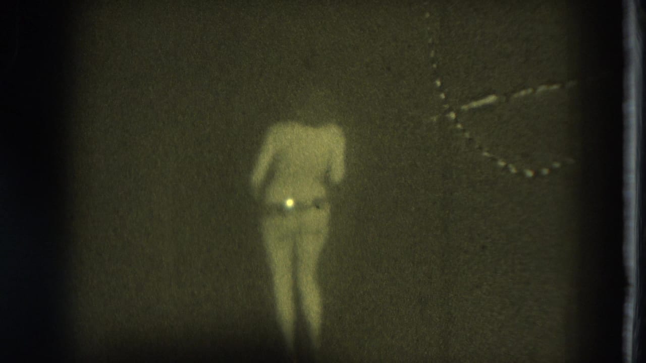 1975 San Francisco 8mm frame showing an adult woman dancing bare-chested in a dim interior with grain and a vertical film edge.