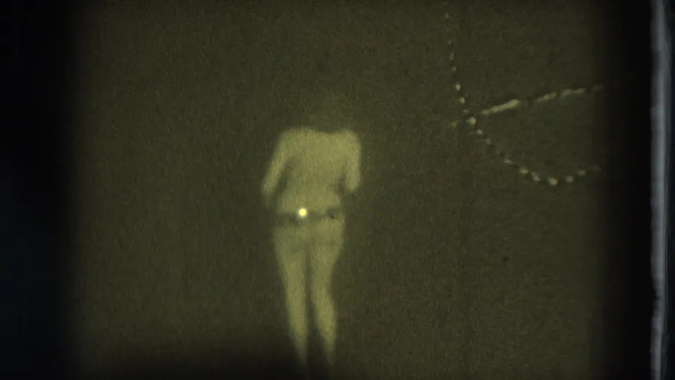 1975 San Francisco 8mm frame showing an adult woman dancing bare-chested in a dim interior with grain and a vertical film edge.