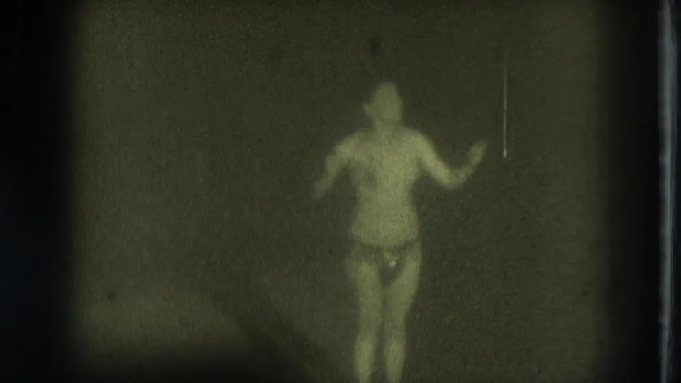 1975 San Francisco 8mm still showing an adult woman dancing toward the camera with one arm lifted in a dim room.