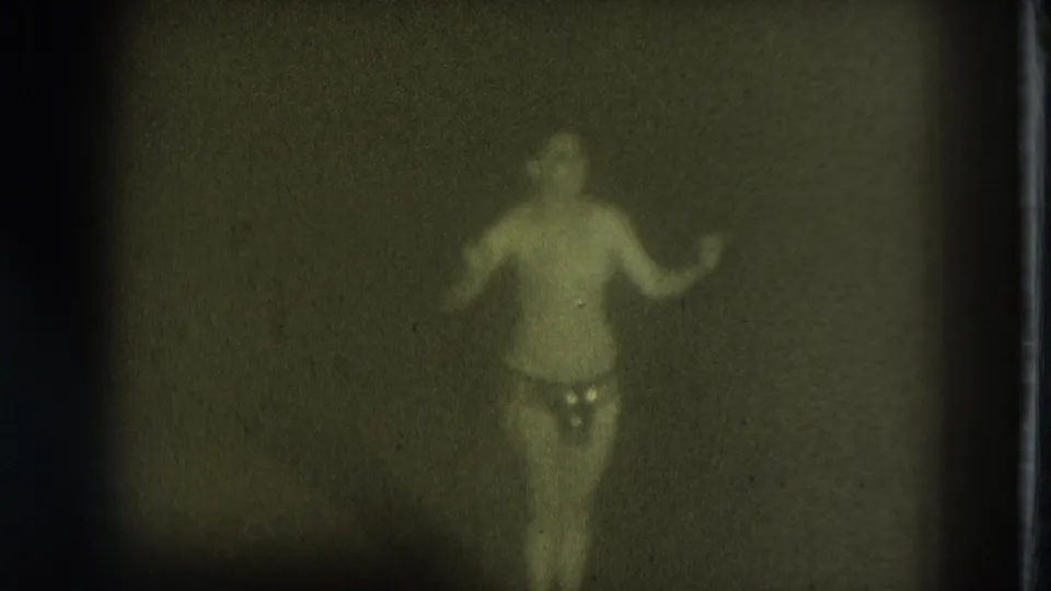 1975 San Francisco 8mm frame showing a dimly lit adult-stage performer in minimal attire, softened by grain and low light.