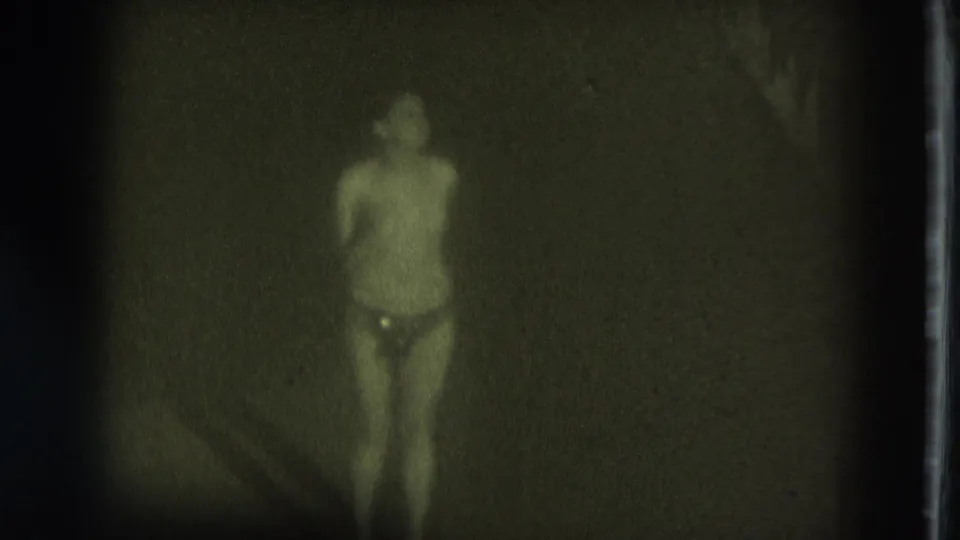 1975 San Francisco 8mm frame of a performer facing the camera in low light, with heavy grain and a dark stage background.