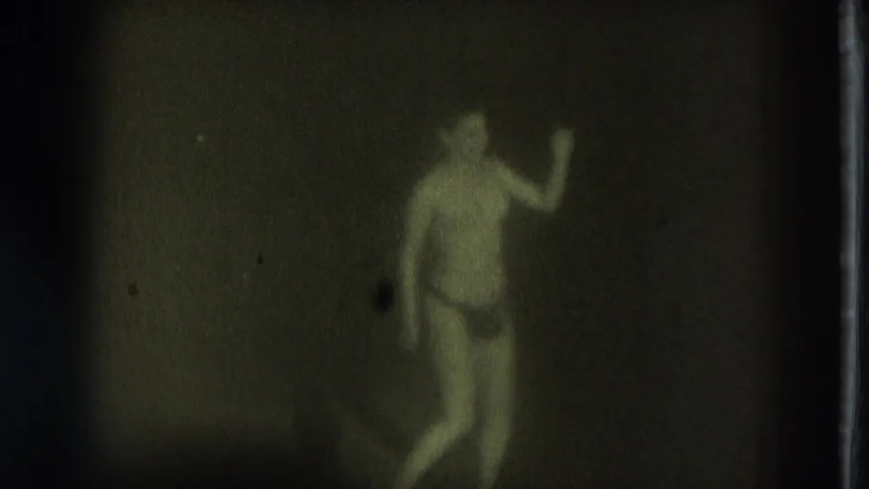 1975 San Francisco 8mm frame of a dimly lit performer at frame right, arm raised during an adult-stage dance.