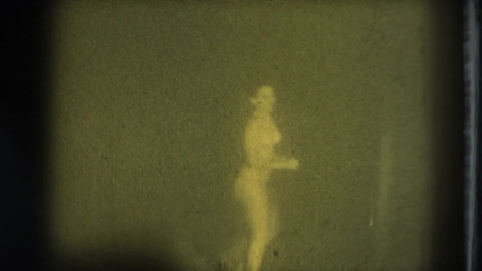 1975 San Francisco 8mm frame showing a side view of a minimally clothed performer in hazy, green-tinted low light.