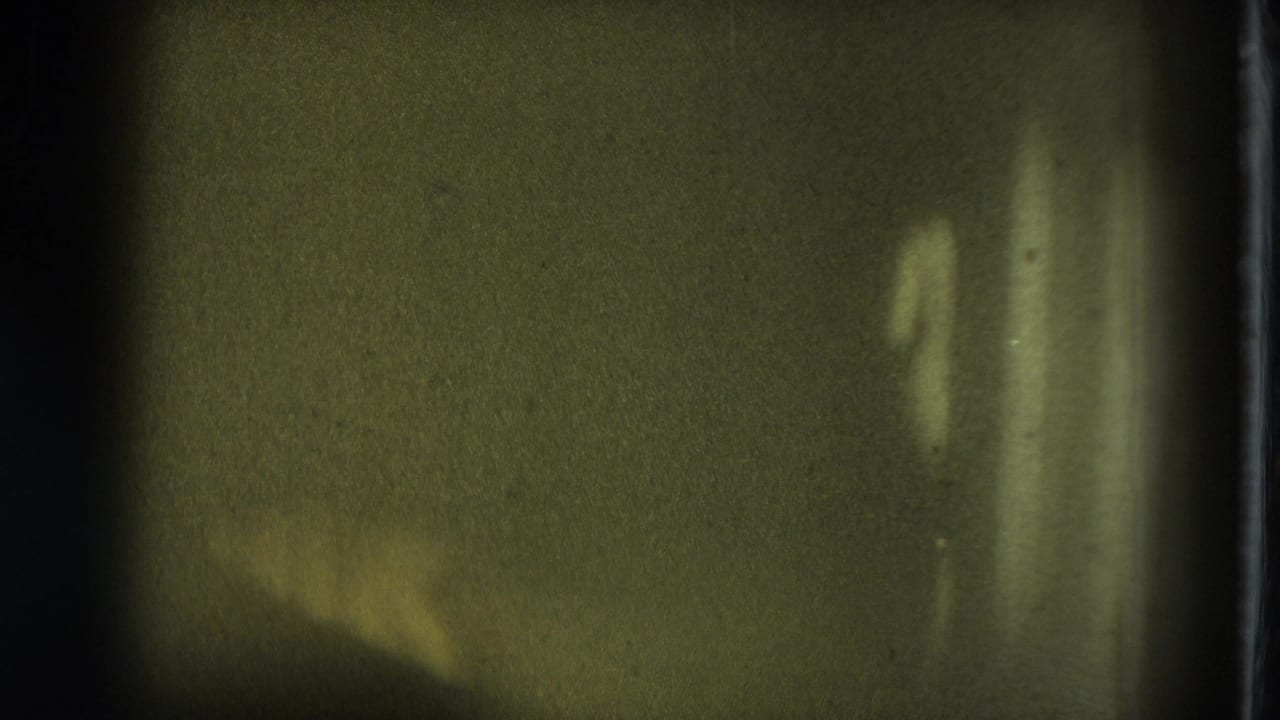 Dark green-tinted frame with indistinct light shapes and vertical film borders.