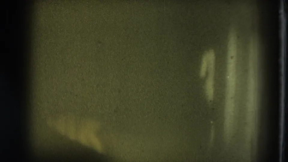 1975 San Francisco 8mm frame with heavy grain, dark borders, and faint shapes in a dim interior.