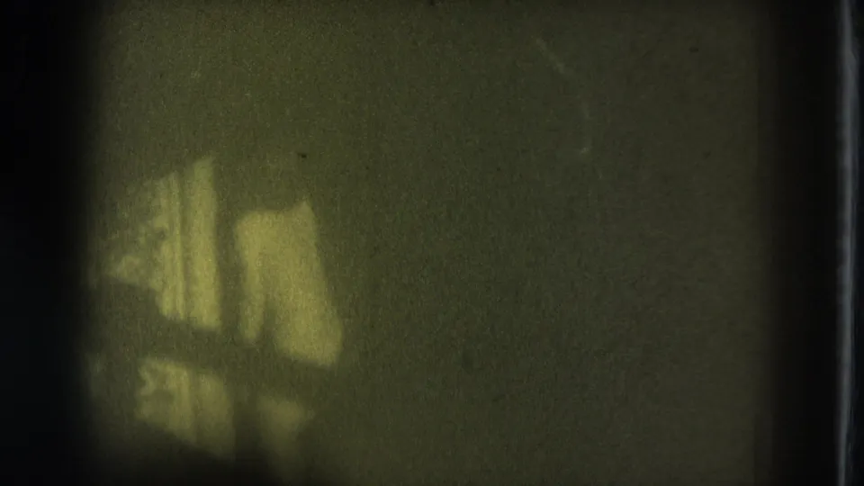 Grainy 1975 San Francisco 8mm frame with an indistinct adult figure shape in a dim room.