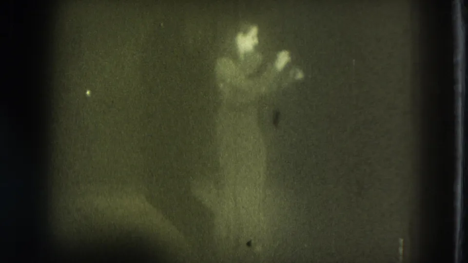 1975 San Francisco 8mm frame showing a distant, blurred stage performer under dim light with strong grain and green-yellow cast.