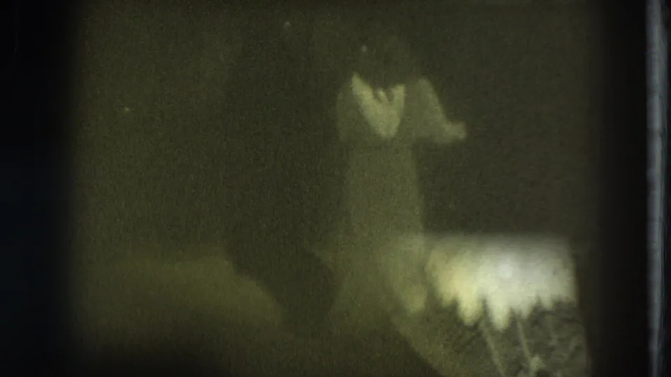 1975 San Francisco home-movie frame showing a distant stage performer with a pale costume area and pronounced grain.