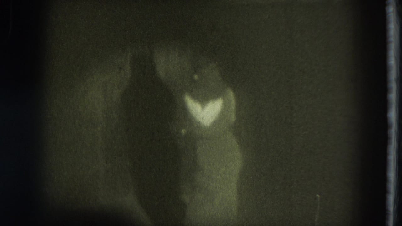 A dancer in a pale dress stands on a dim stage under greenish light.