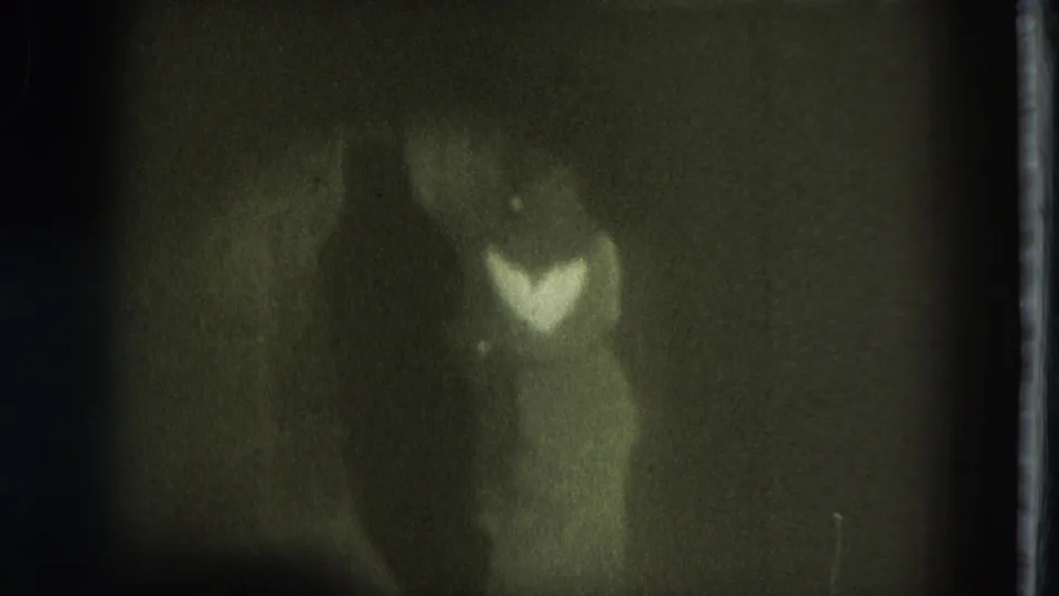 1975 San Francisco home-movie frame showing a dancer in a pale dress on a dark, softly focused stage.
