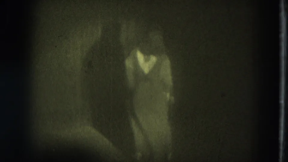 Soft 8mm frame from 1975 San Francisco showing a stage dancer in low light from a fixed audience-side view.