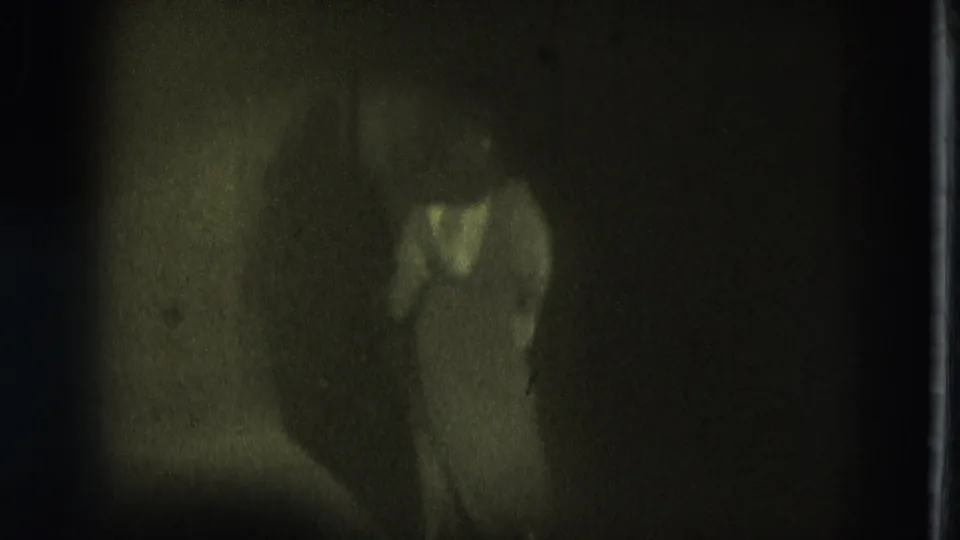 1975 San Francisco home-movie still showing the dancer low in frame under dim greenish stage light.