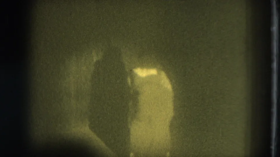 Low-light 8mm frame from San Francisco in 1975 with a performer moving under a yellow-green spotlight.