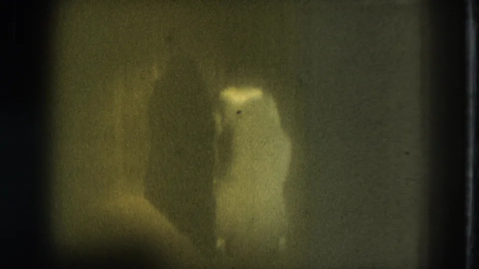 1975 San Francisco home-movie frame showing a soft, shadowy performer in a dim performance area.