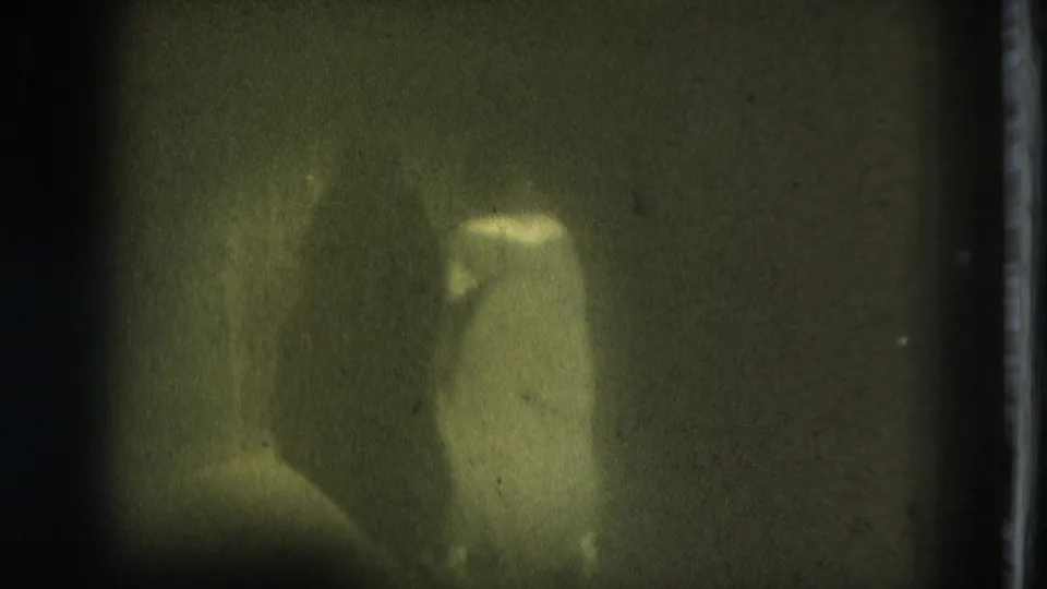 Green-tinted 8mm frame of a performer in light clothing moving against a dark background in 1975 San Francisco footage.
