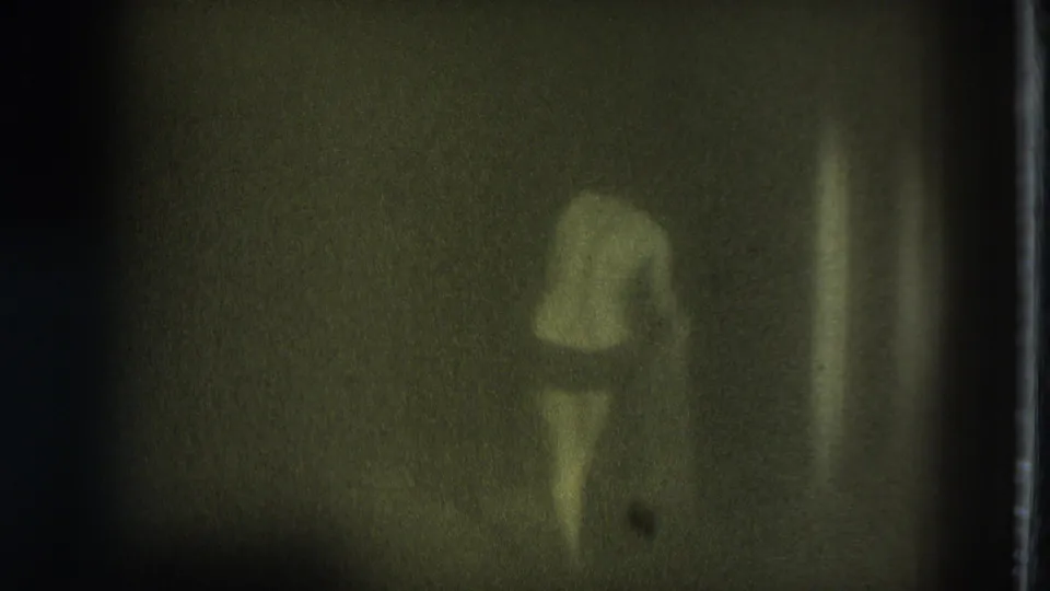 Adult woman in underwear moves away from the camera in a dim, green-tinted 8mm frame.