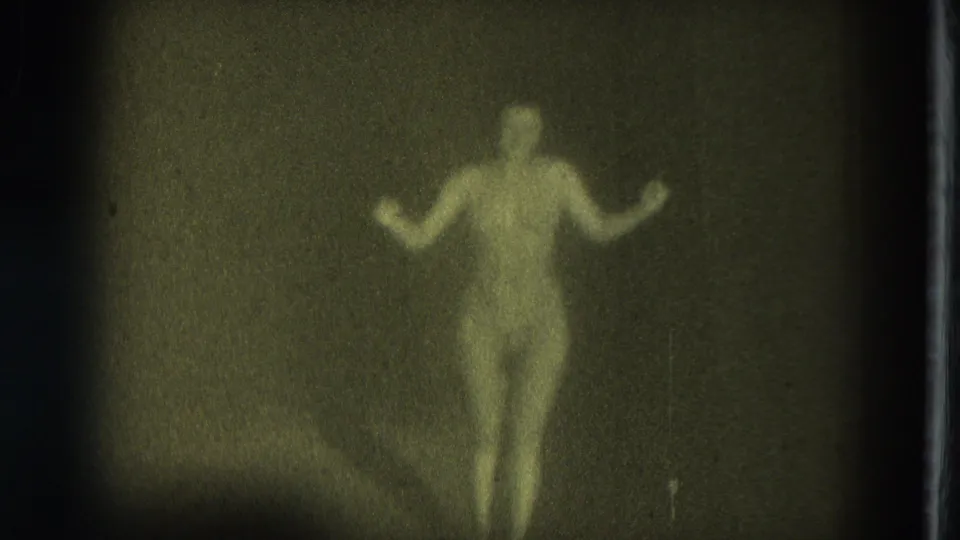 The performer walks toward the camera area with both arms out, softly rendered by grain and low light in the 1975 San Francisco clip.