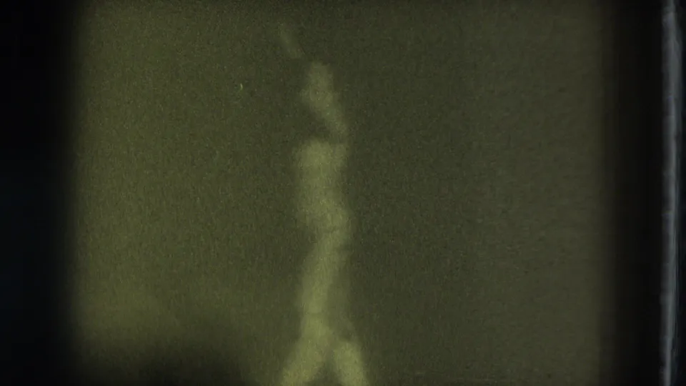 A soft side-profile view shows the nude adult woman moving or posing in the dim 1975 San Francisco 8mm home-movie footage.